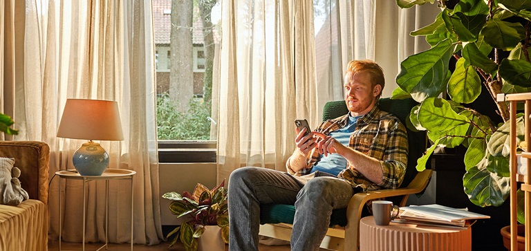 Man zit ontspannen op de bank in een woonkamer en gebruikt zijn smartphone, symbool voor gemak bij het regelen van energie via ENGIE